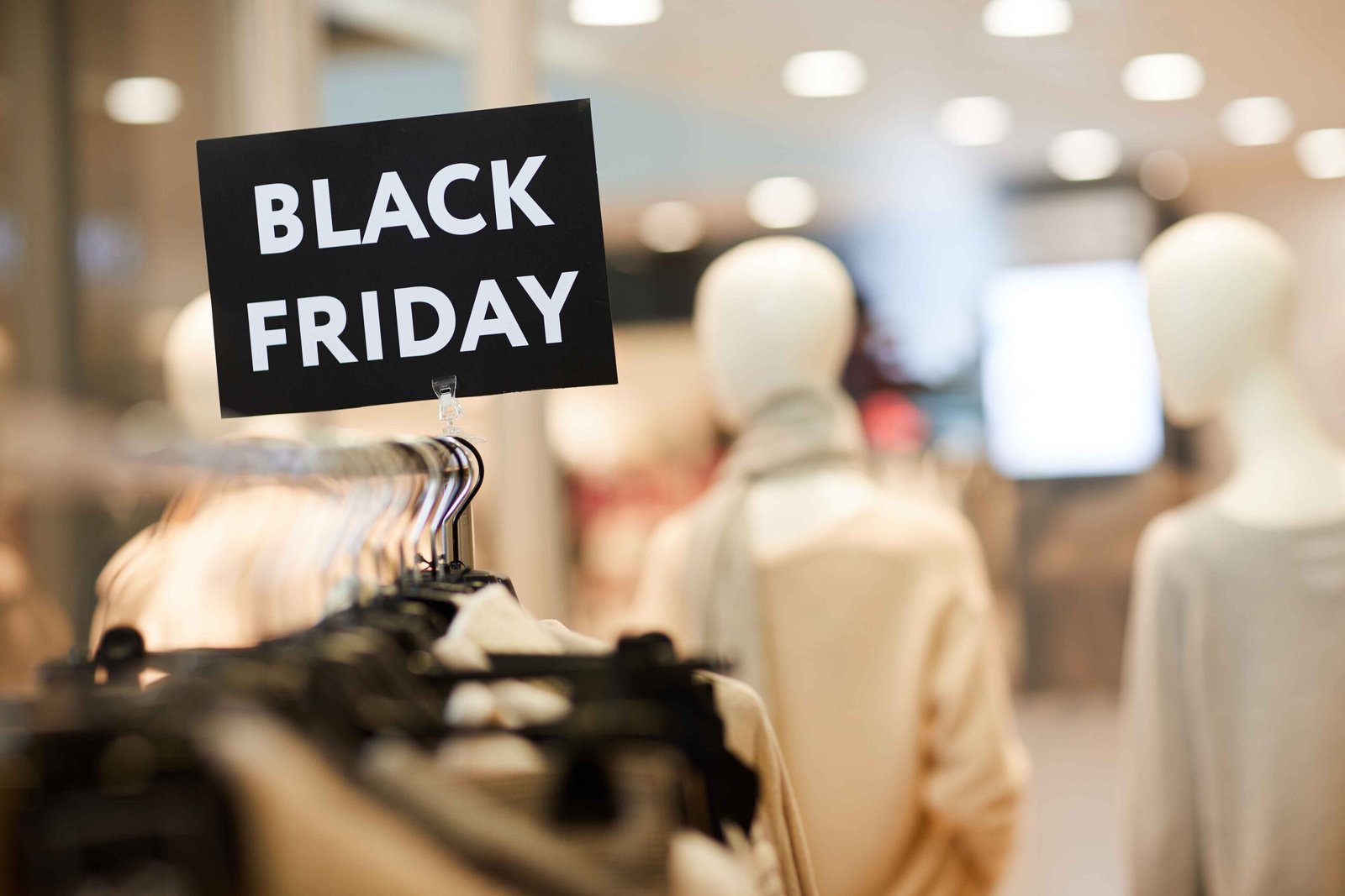 Background image of Black Friday sign on clothes rack with autumn clothes in shopping mall during sale season, copy space